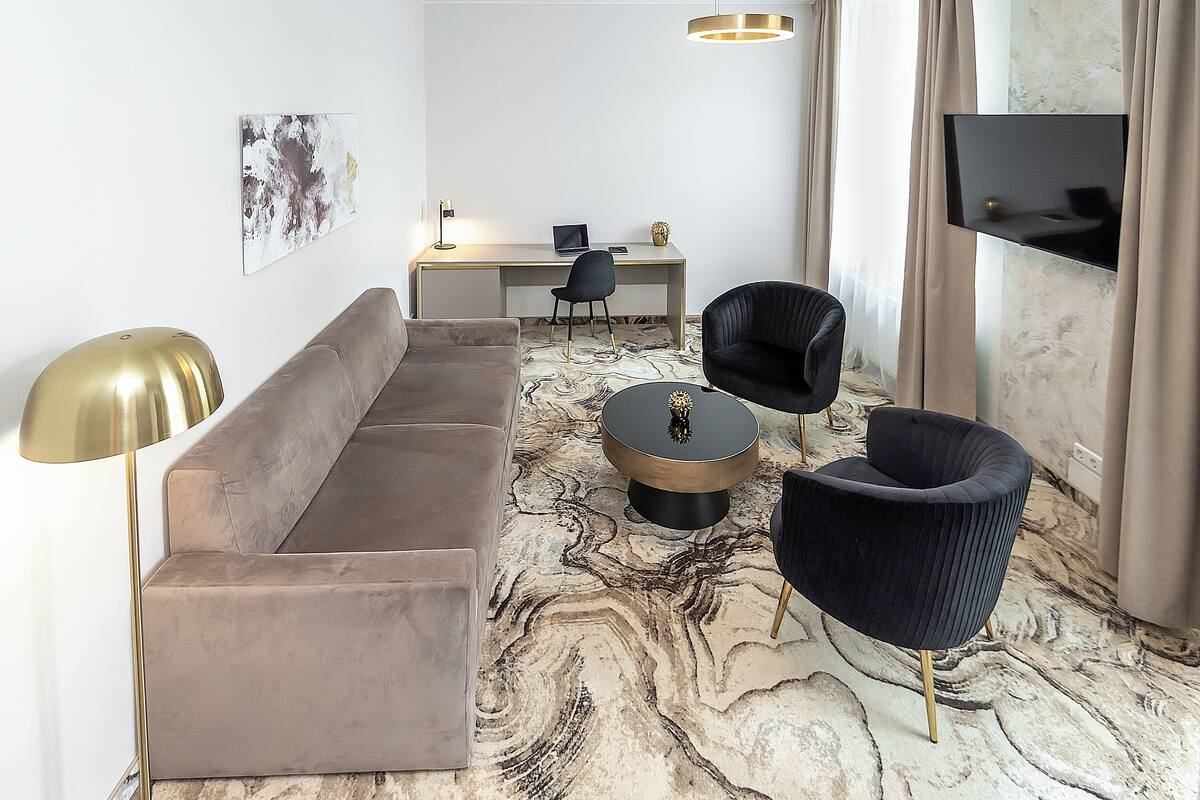 A modern living room with a sofa, two chairs, a coffee table, a desk with a computer, and a TV mounted on the wall.