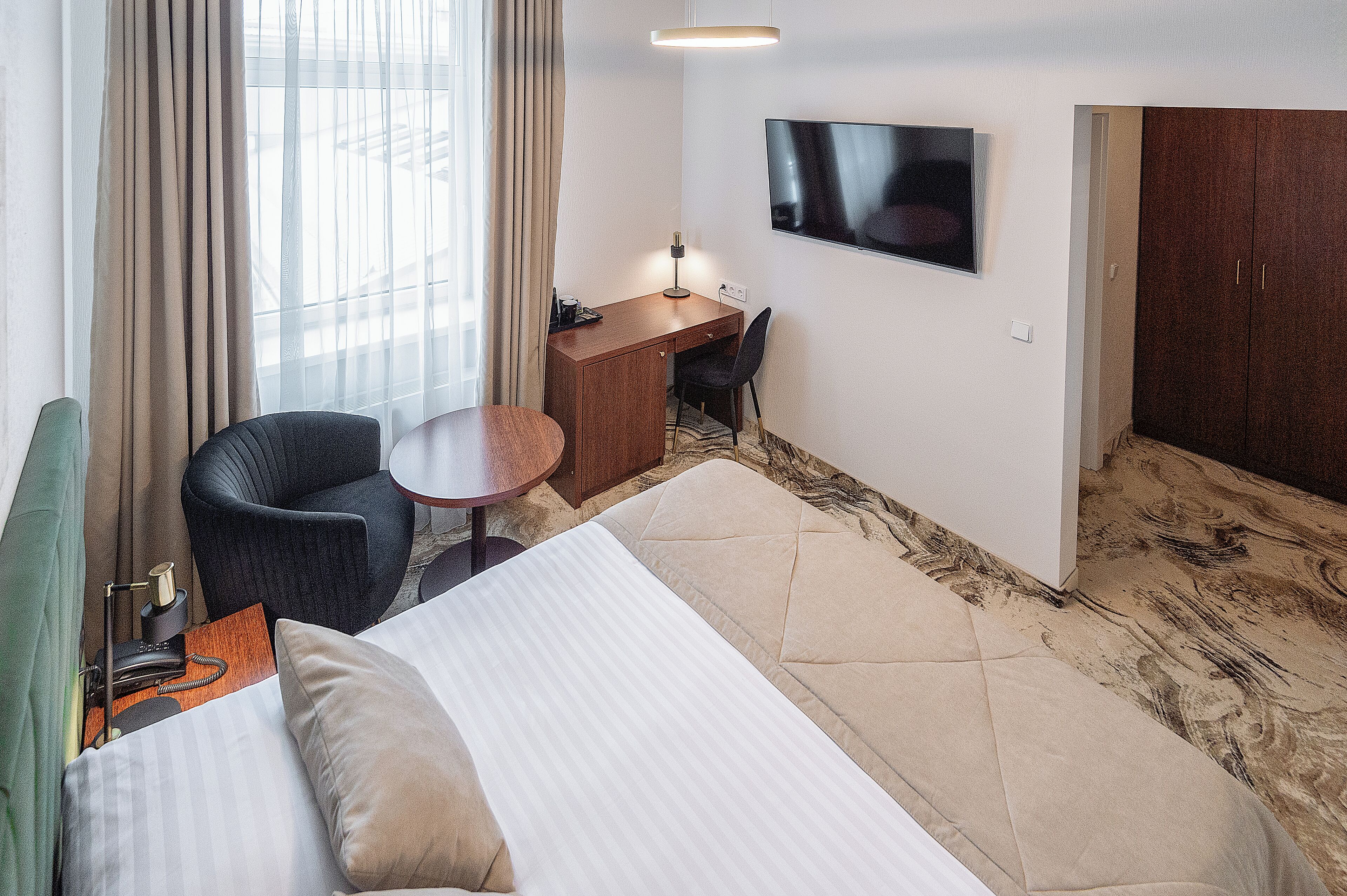 A hotel room with a bed, a desk, a chair, a TV, and a wardrobe.