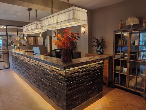 A reception area with a stone counter, a large chandelier, and a cabinet with glass doors. - Cocoon Hotel Belair (Bourscheid)