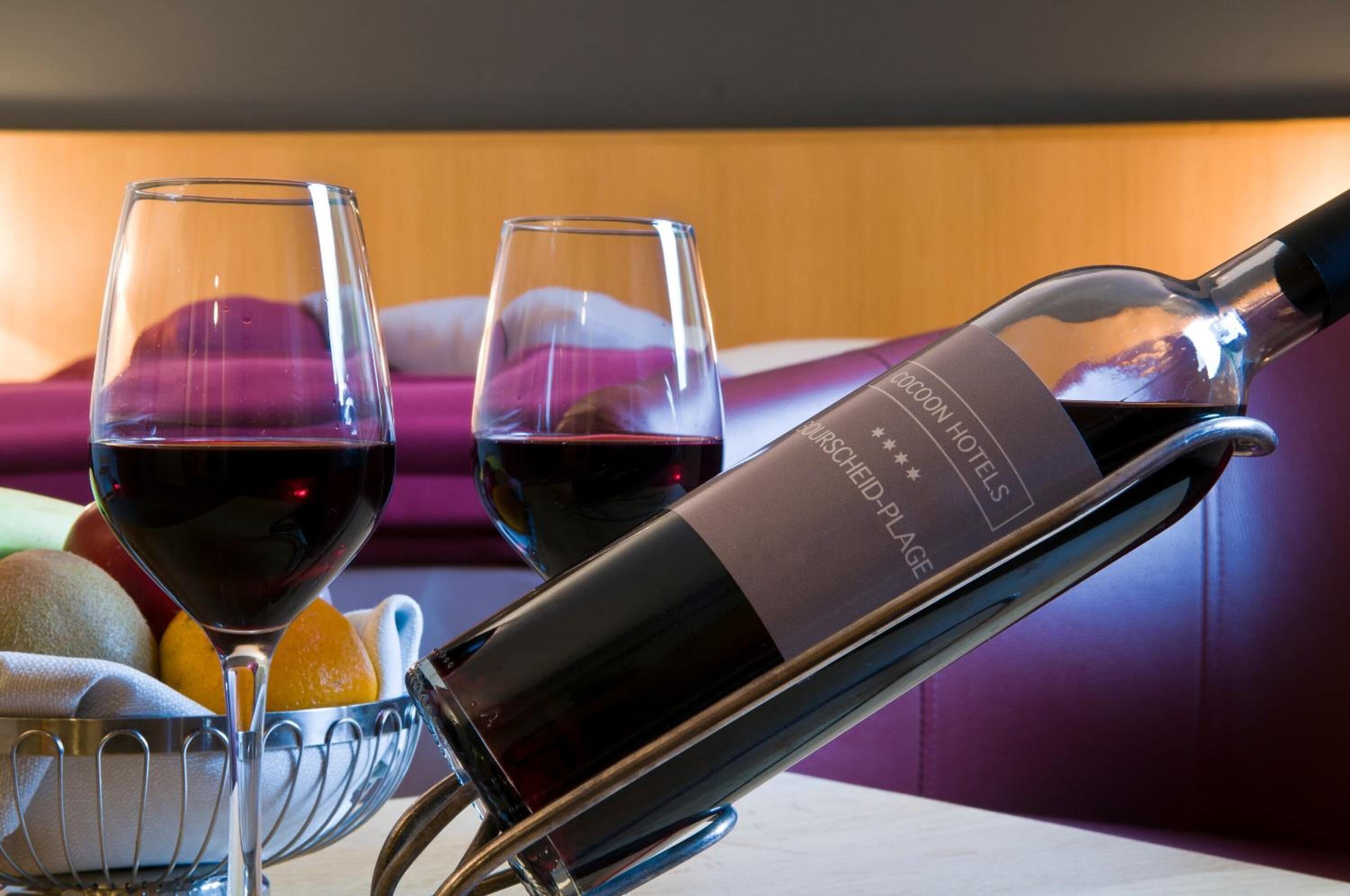 A bottle of wine, two wine glasses, and a fruit basket on a table.