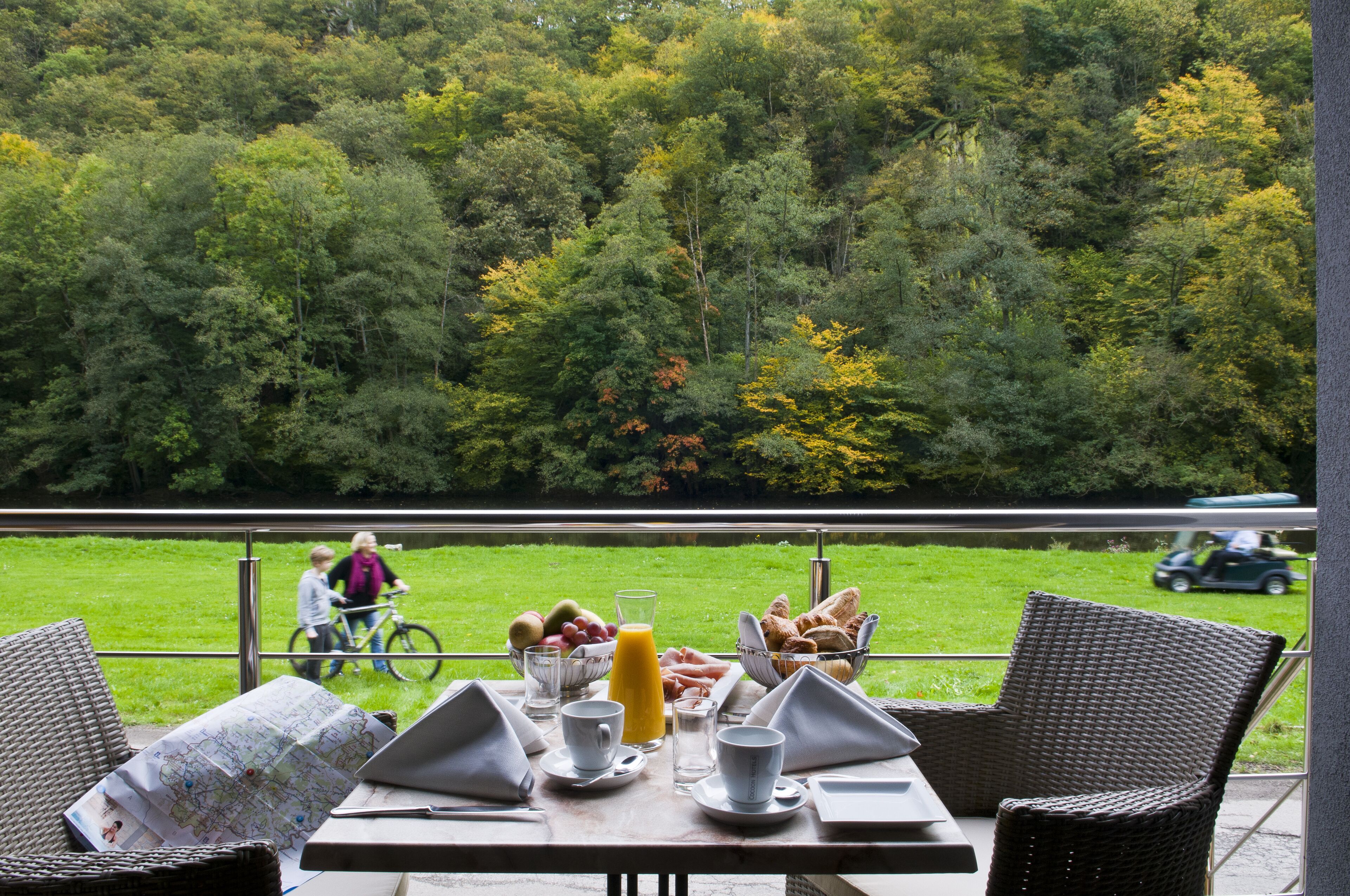 Une table de petit-déjeuner dressée avec une carte, des boissons et de la nourriture, donnant sur une zone herbeuse et des arbres.