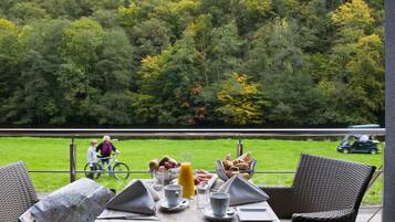 Une table de petit-déjeuner dressée avec une carte, des boissons et de la nourriture, donnant sur une zone herbeuse et des arbres.