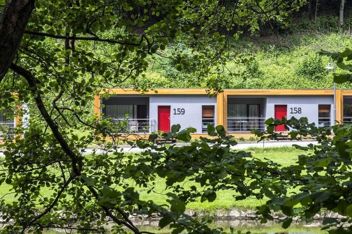 Duas cabanas, números 159 e 158, com porta vermelha, em meio a um ambiente verde exuberante.