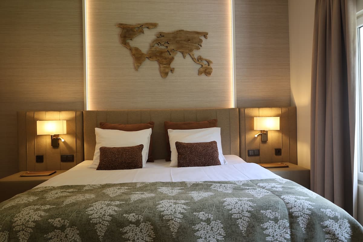 Cama bem arrumada com arte de parede de mapa mundi, duas luminárias de cabeceira e um edredom floral verde.