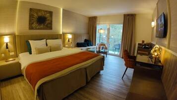 A hotel room with a large bed, a desk, a chair, a balcony, and a television.