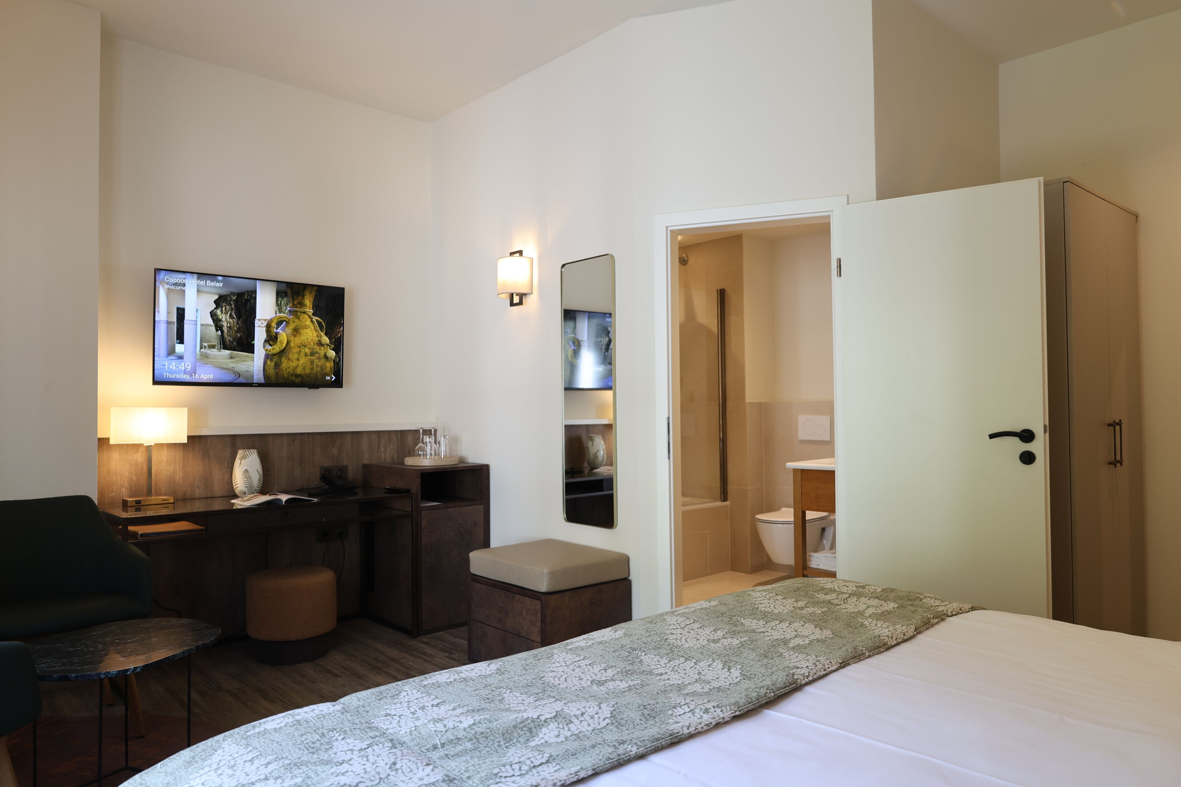 A hotel room with a bed, a desk, a chair, a TV, a mirror, and a wardrobe.