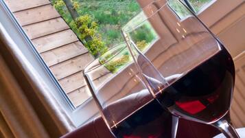 Deux verres à vin sont posés sur une table près d’une fenêtre donnant sur des arbres et une terrasse en bois.