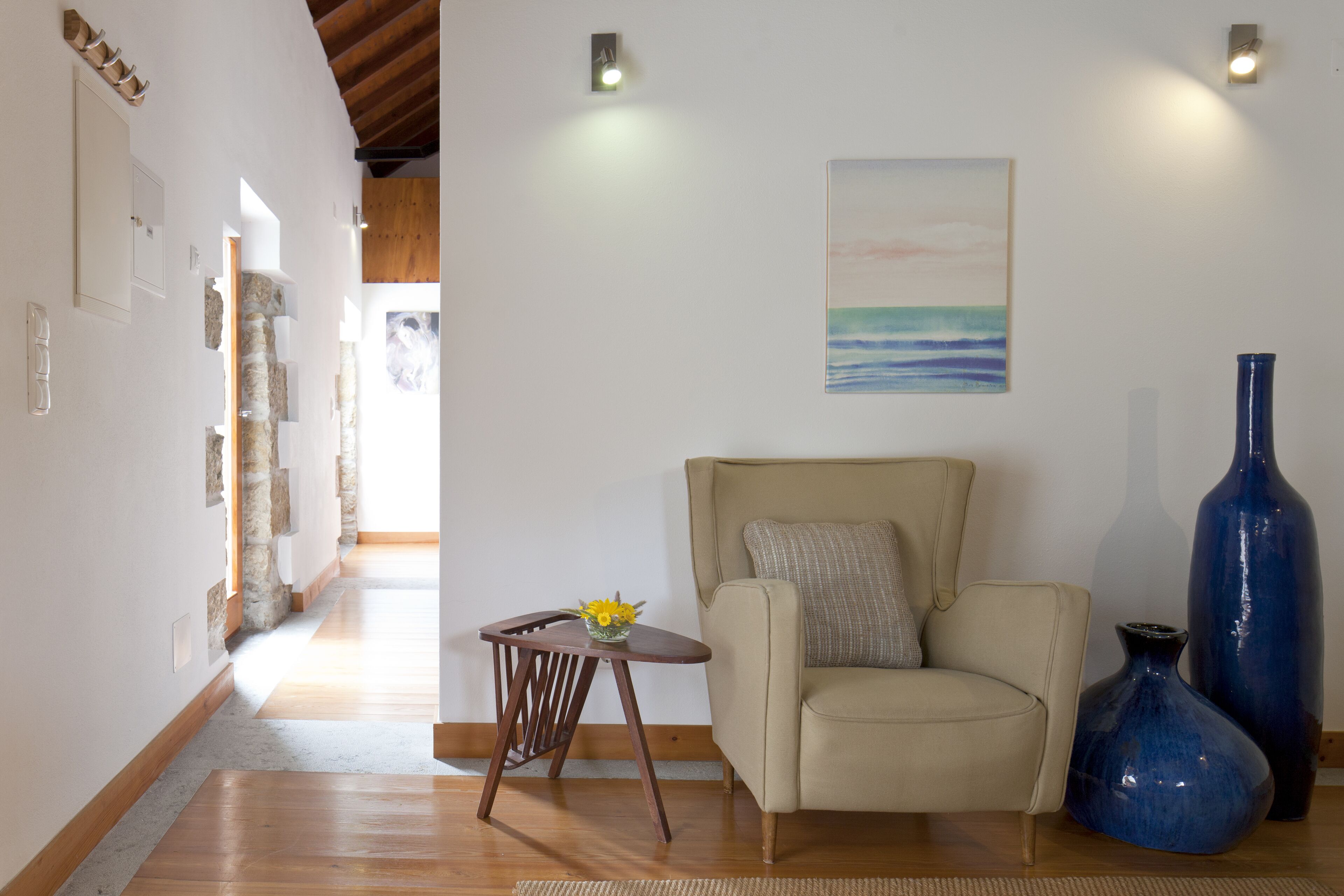 Una sala de estar con un sofá color beige, una pequeña mesita de madera con un jarrón y un cuadro en la pared.