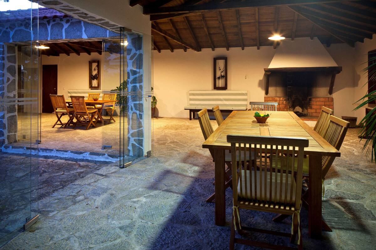 A dining area with a stone floor, wooden table, and chairs, a stone wall, and a fireplace.