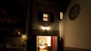 A nighttime view of a building with a lit entrance, a small window, and a stone wall. - Solar do Magoito (Sintra)