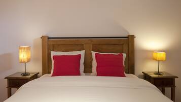 Una cama bien hecha con tablero de madera, dos almohadas rojas y dos lámparas de noche sobre mesitas de madera.
