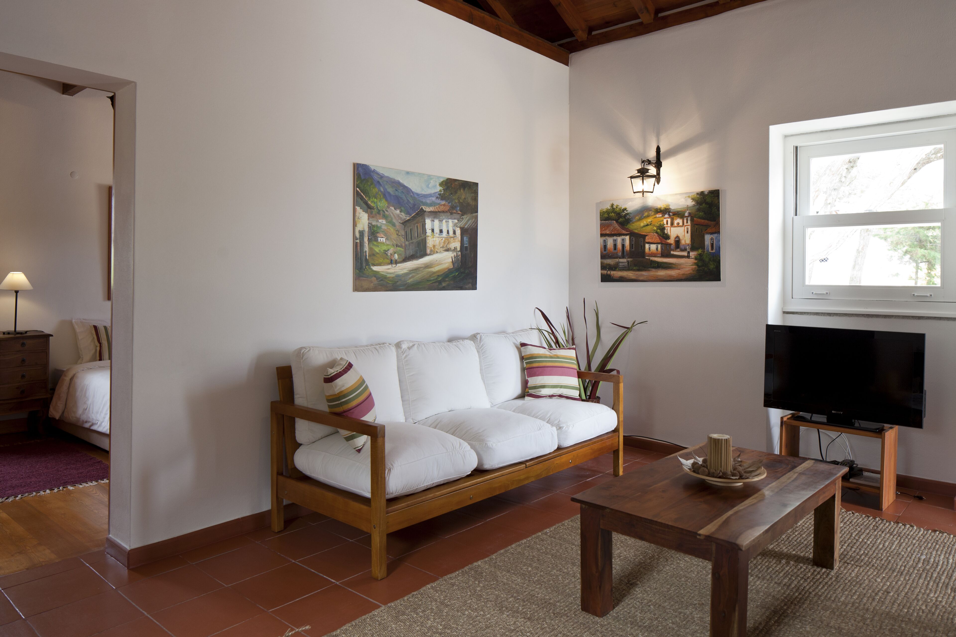A living room with a white sofa, wooden coffee table, and paintings on the wall.