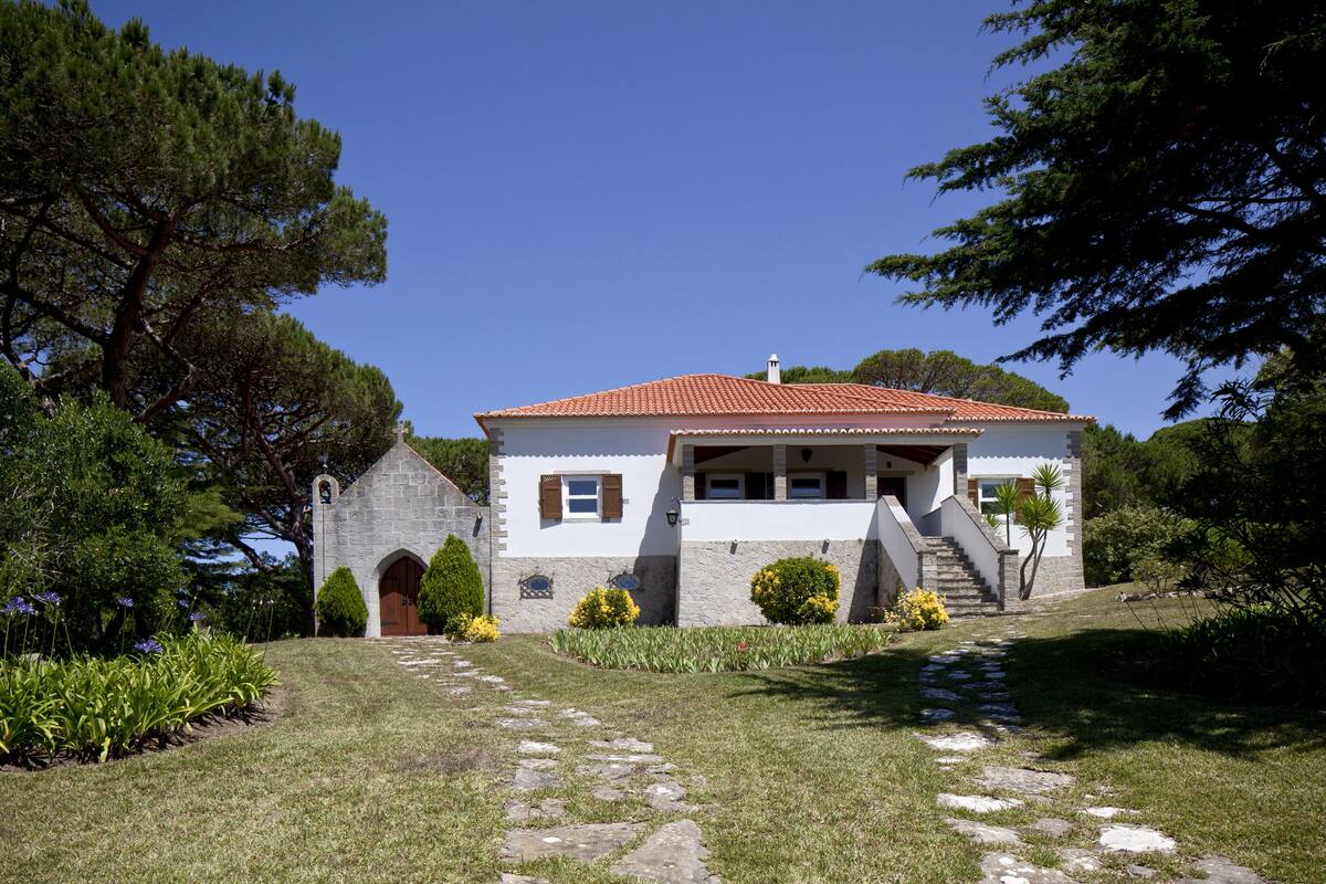 A two-story building with a red-tiled roof, a stone facade, and a small bell tower.