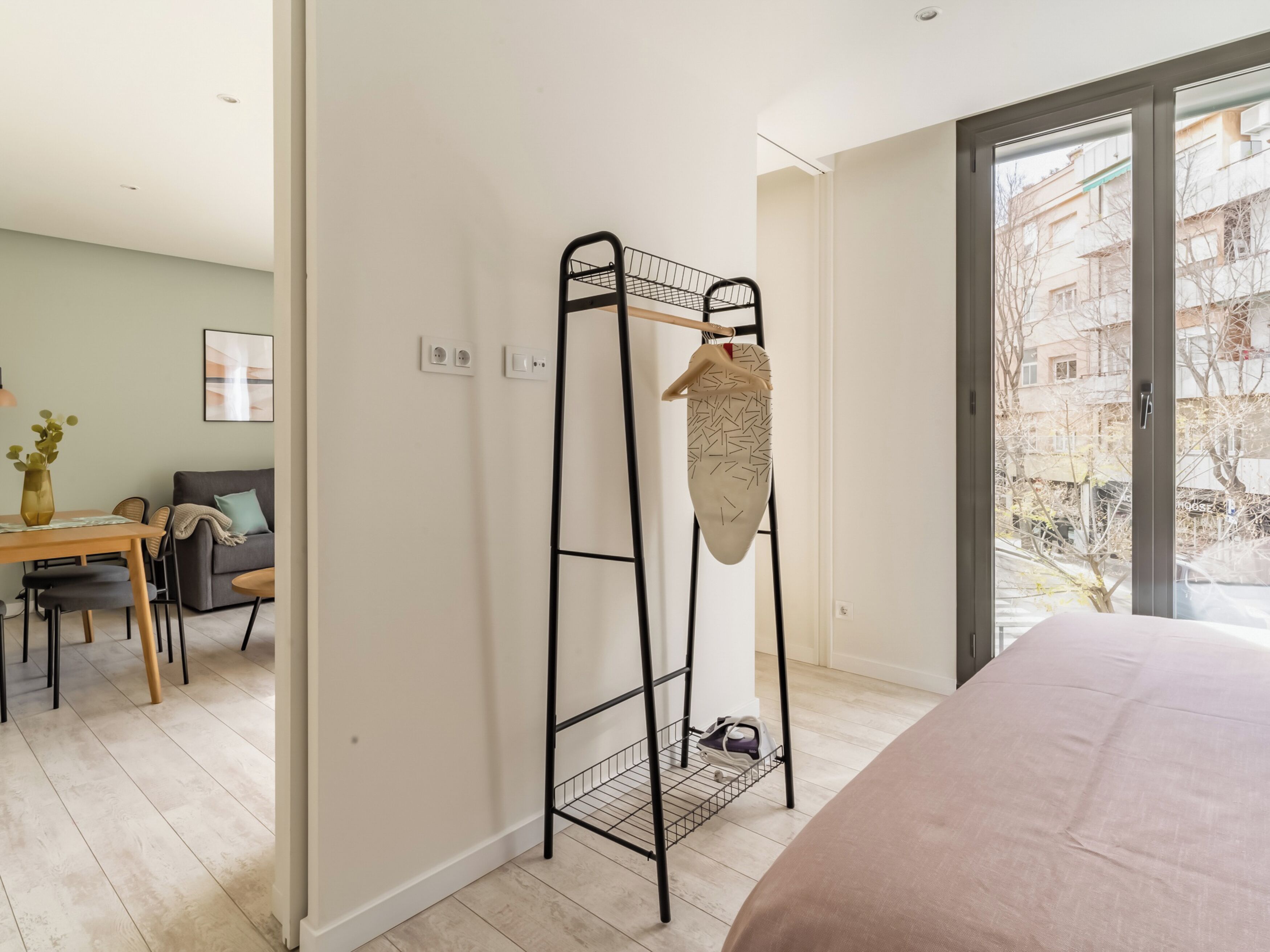 A modern room with a bed, a dining area, and a clothing rack with a garment hanging.