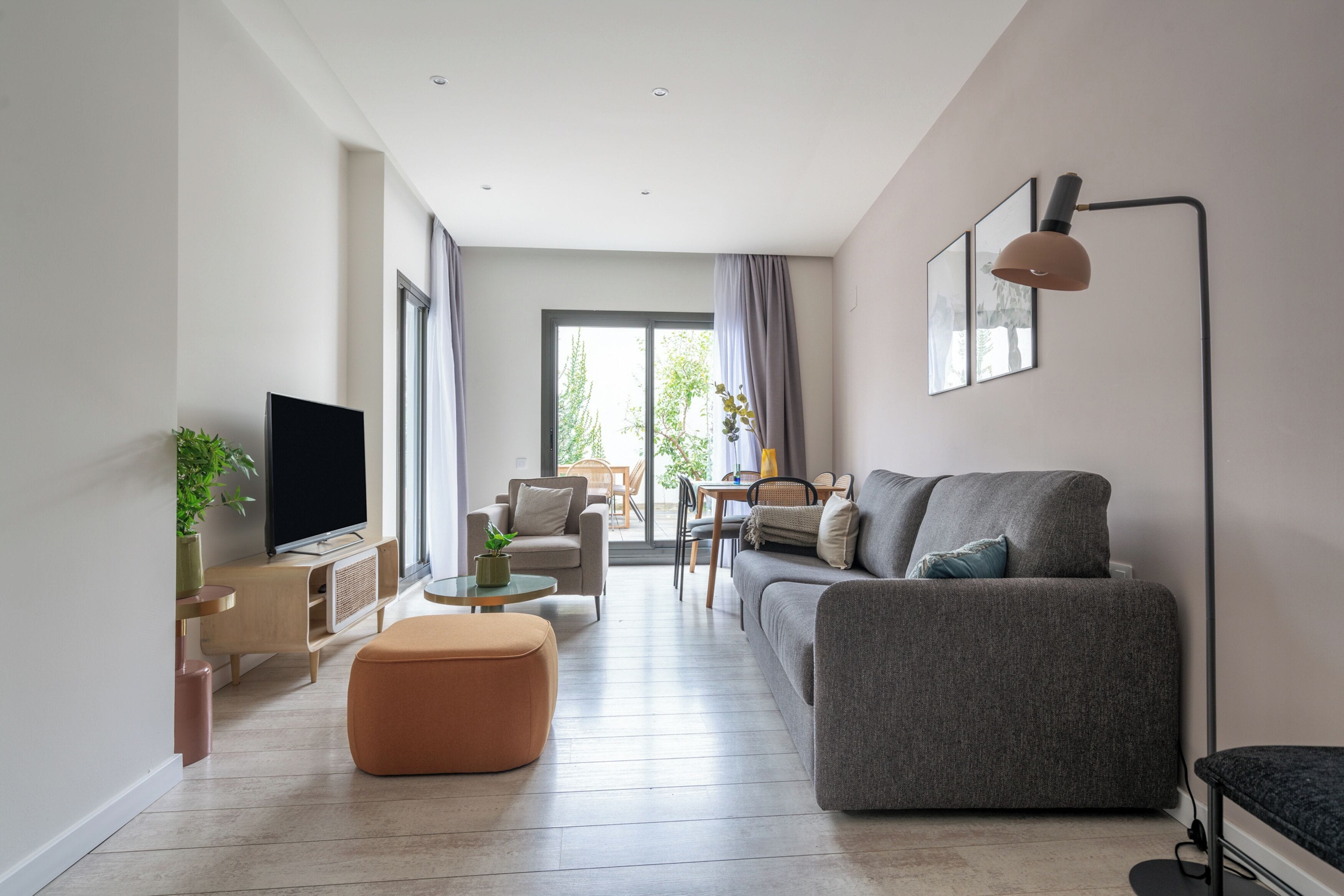 En moderne stue med et fladskærms-tv, en grå sofa, et sofabord og et spiseområde med stole.