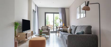 A modern living room with a flat-screen TV, a grey sofa, a coffee table, and a dining area with chairs.