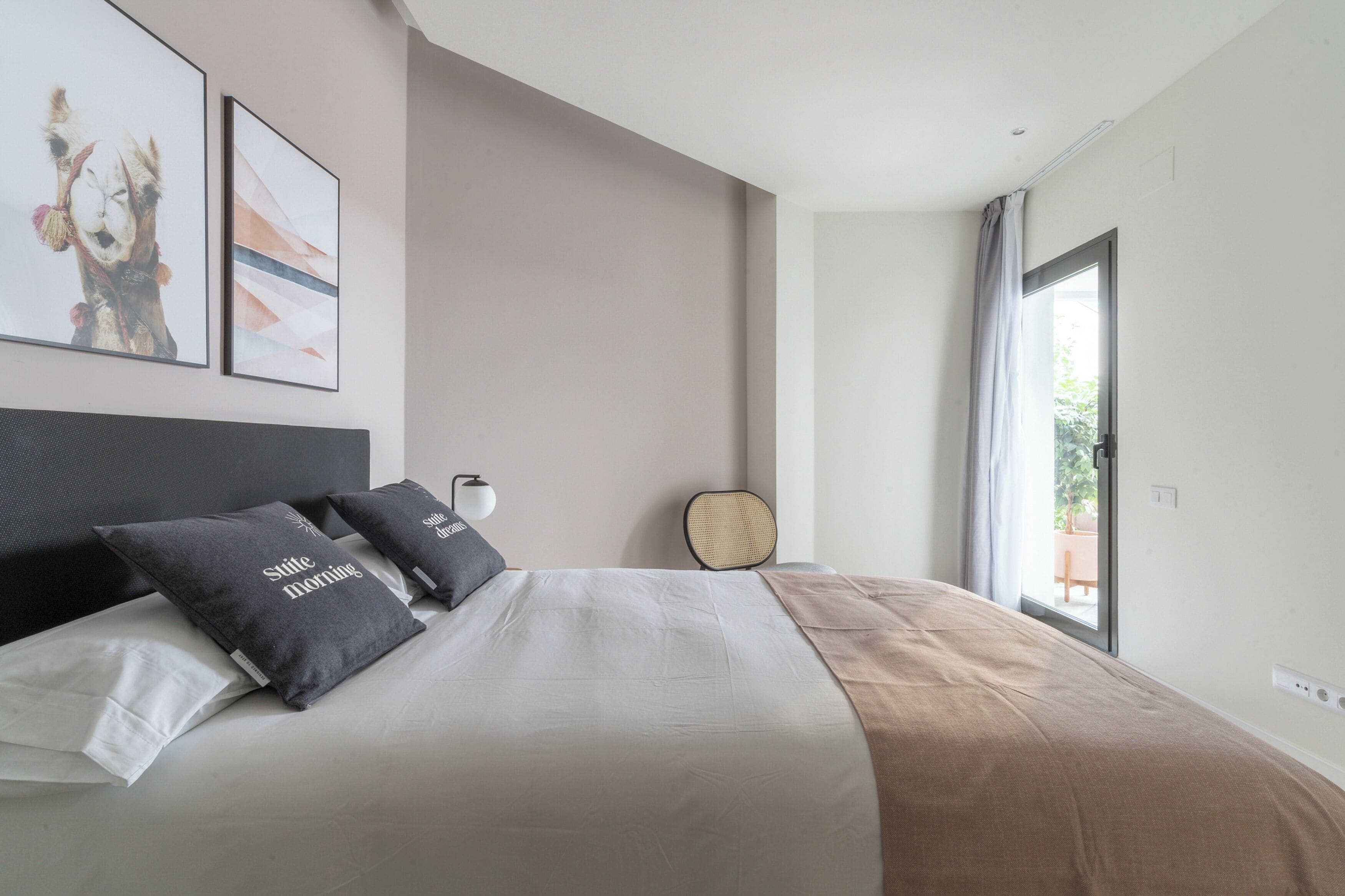 Un dormitorio moderno con una cama grande, dos almohadas, una mesita de noche, una lámpara y vistas al exterior.