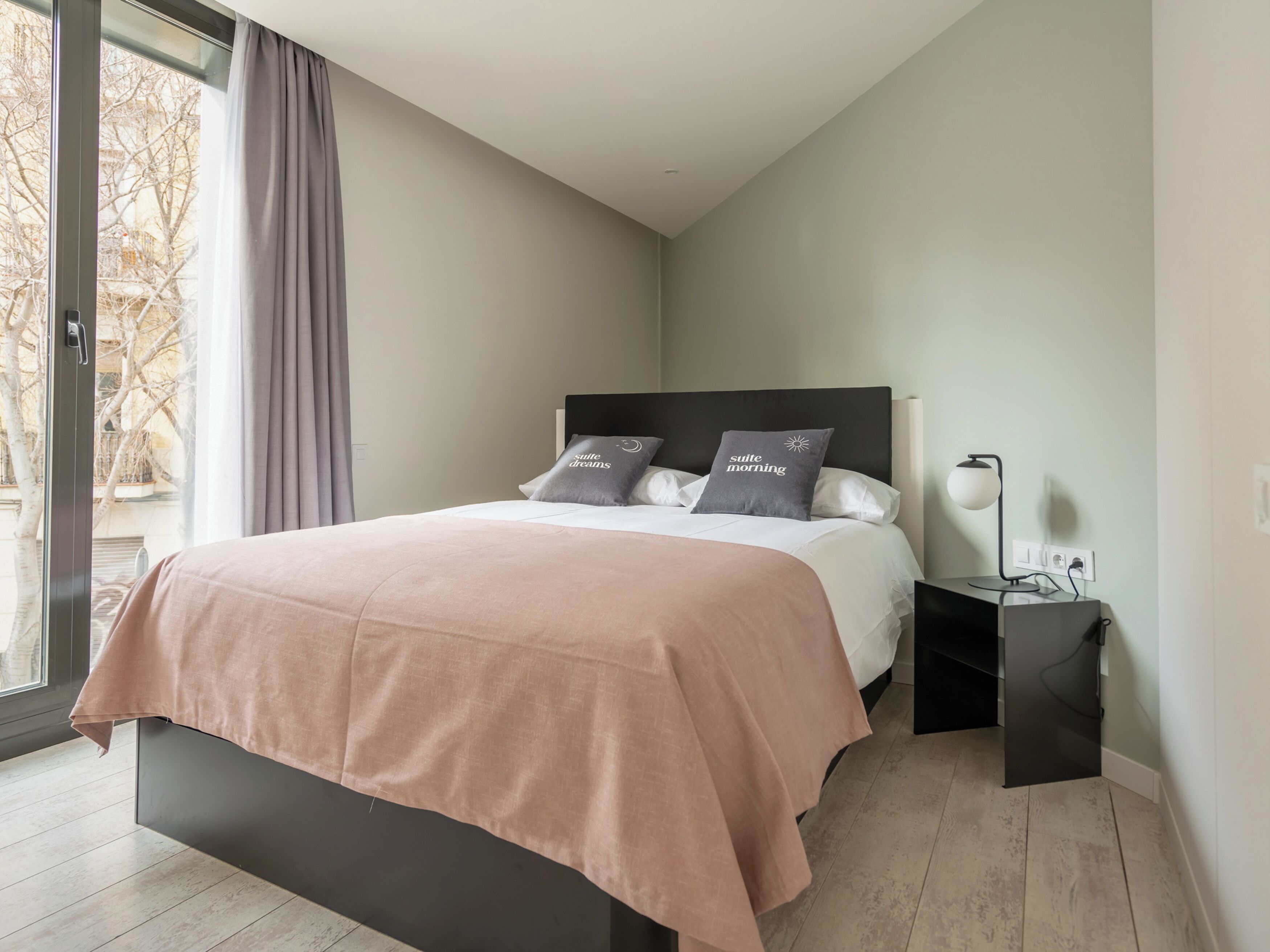 A modern bedroom with a bed, bedside tables, and a view through a window.