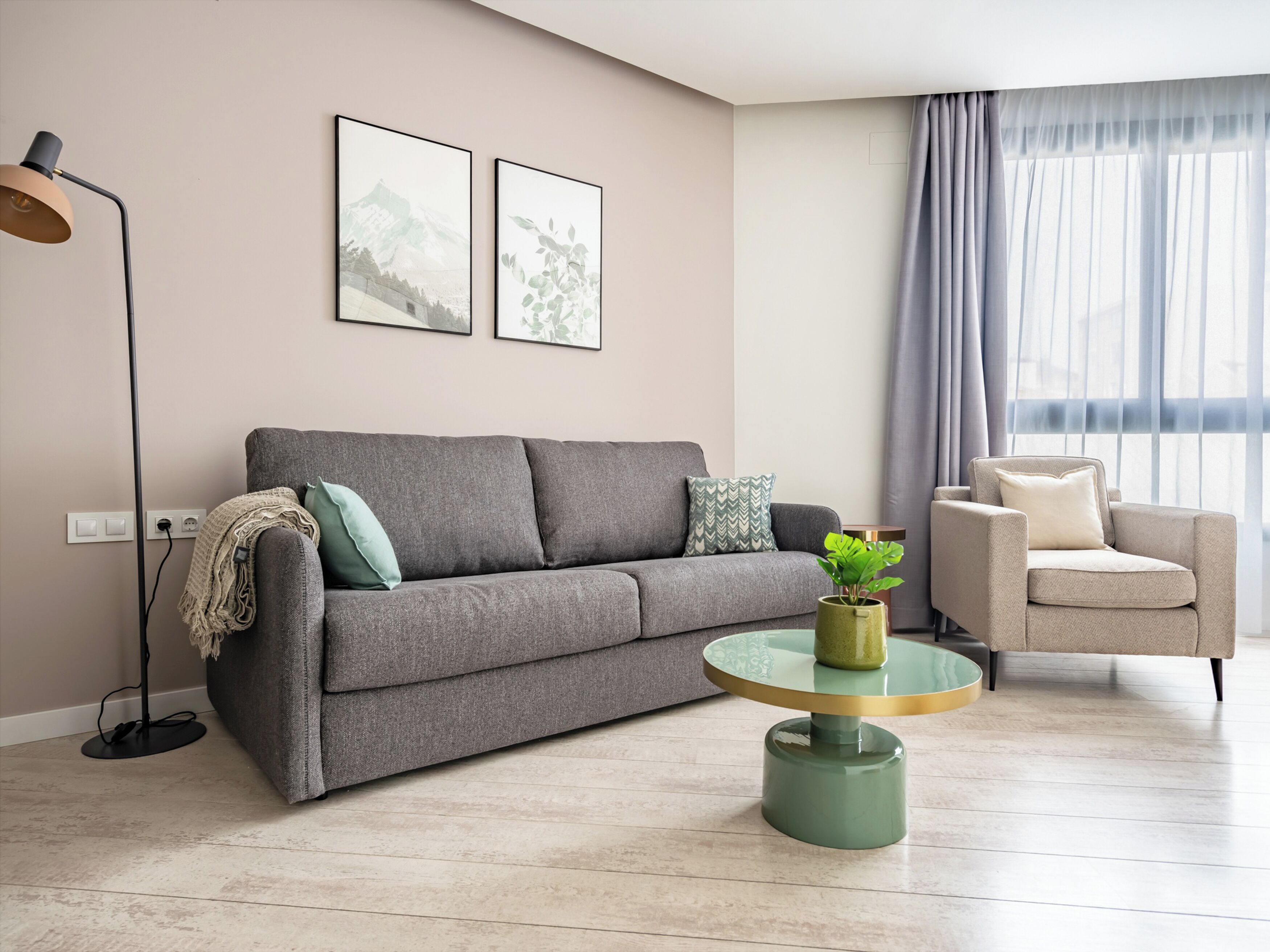 A modern living room with a grey sofa, a round coffee table with a plant, a floor lamp, and a chair.