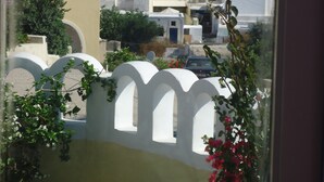 Vista de un pueblo costero con edificios de colores pastel, que incluye una iglesia con cúpulas azules, a través de una ventana con marco blanco y una planta en primer plano.