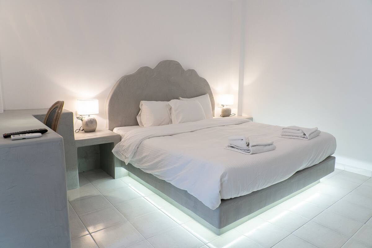 Un dormitorio moderno con una cama grande, lámparas de noche y un control remoto sobre una mesita de noche.