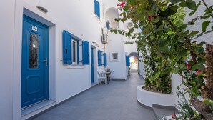 Un callejón estrecho, con paredes blancas, puertas y contraventanas azules, que conduce a una escalera.