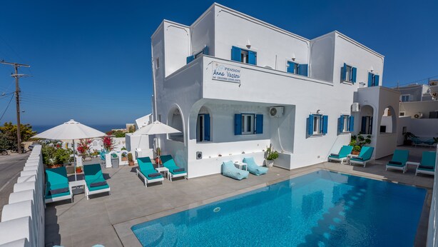 Un edificio blanco con piscina, contraventanas azules y sillones de descanso.