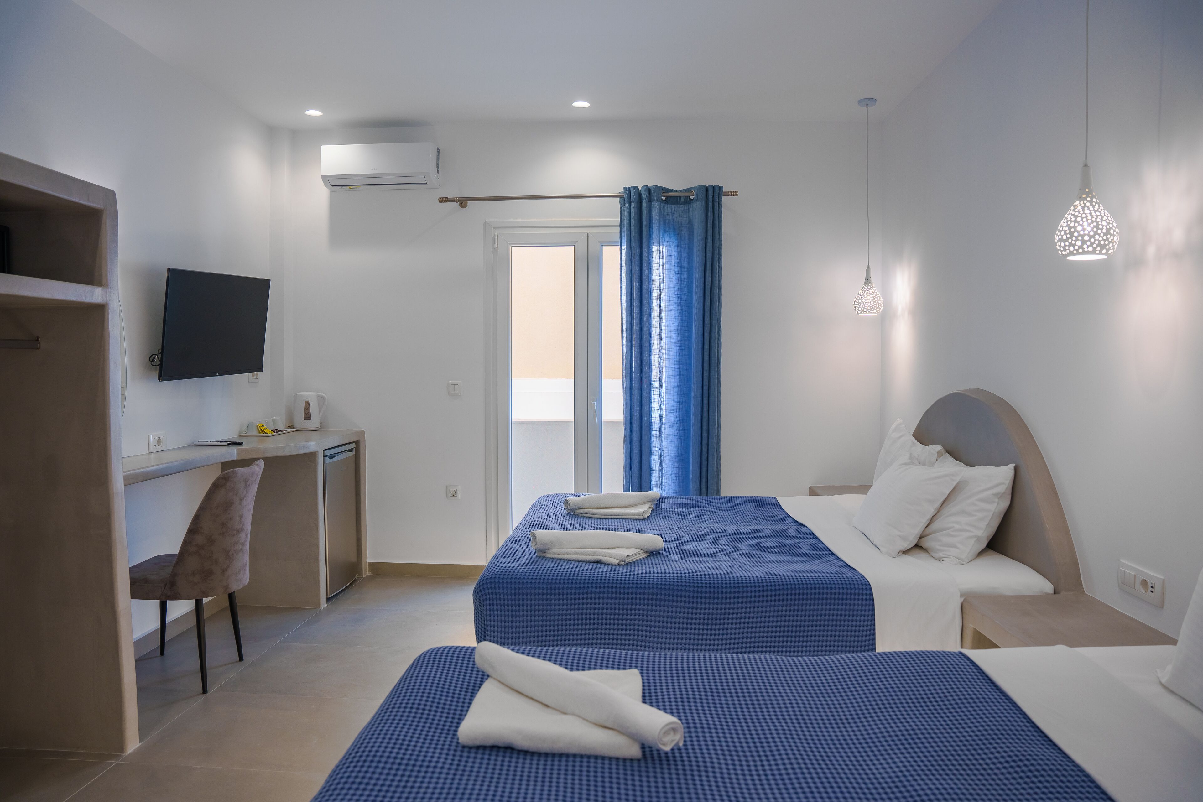 A hotel room with two beds, a desk, a chair, and a TV.