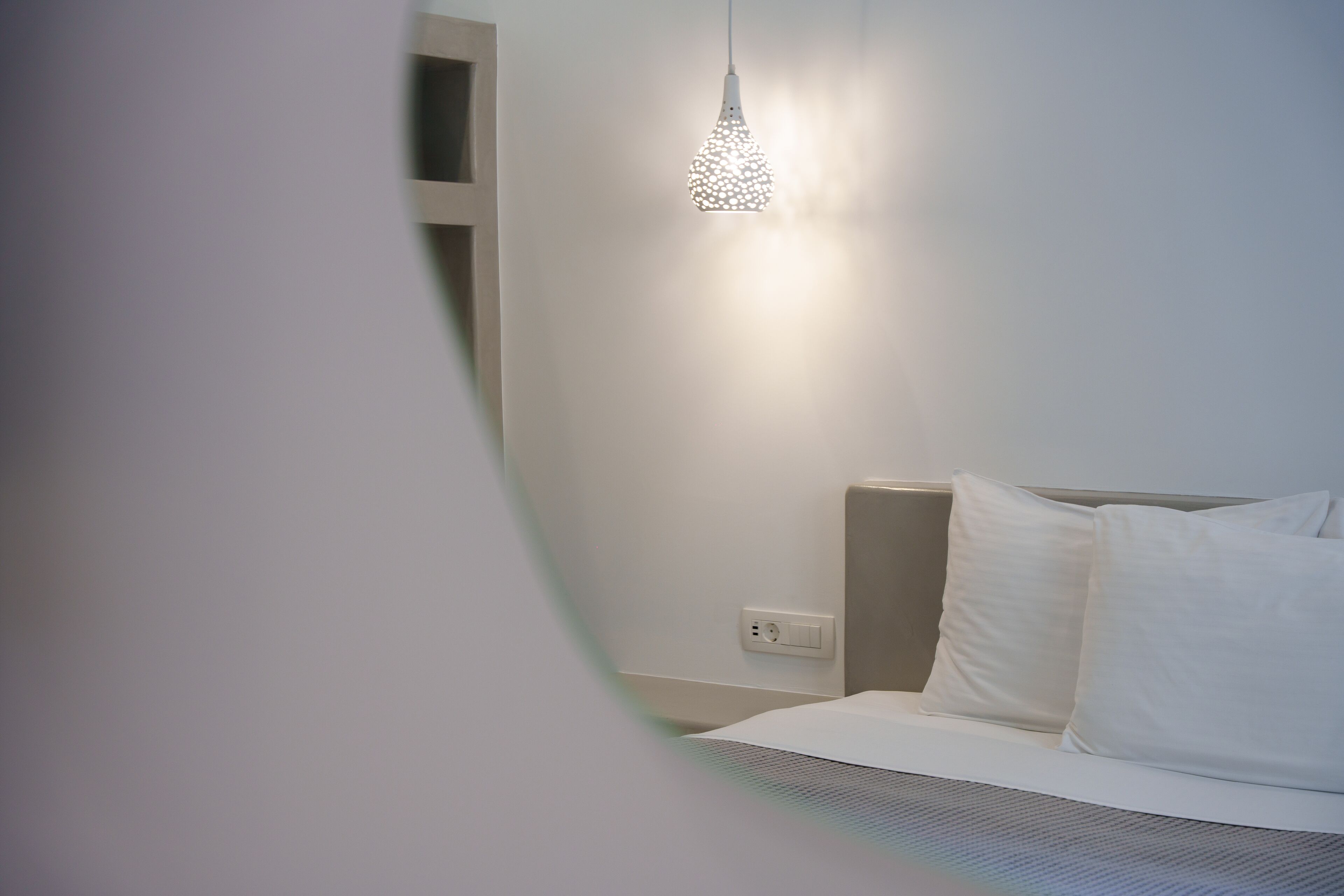 A modern bedroom with a bed, white pillows, and a hanging light fixture.