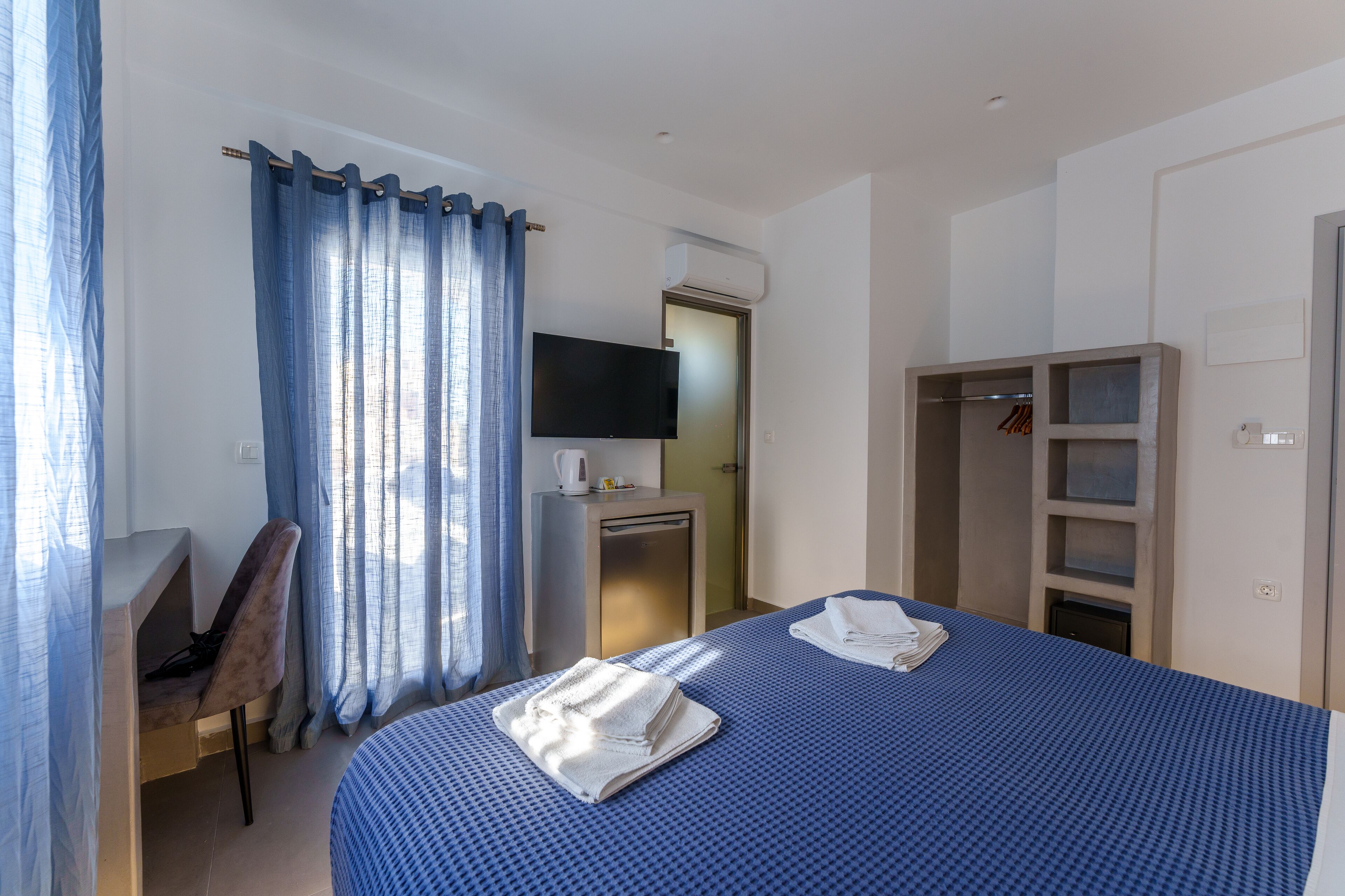 A hotel room with a bed, a desk, a chair, a TV, and a wardrobe.
