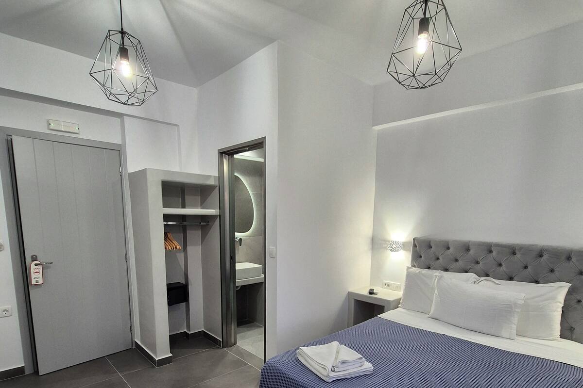 Habitación de hotel moderna con una cama grande, un armario, un baño e iluminación geométrica en el techo.