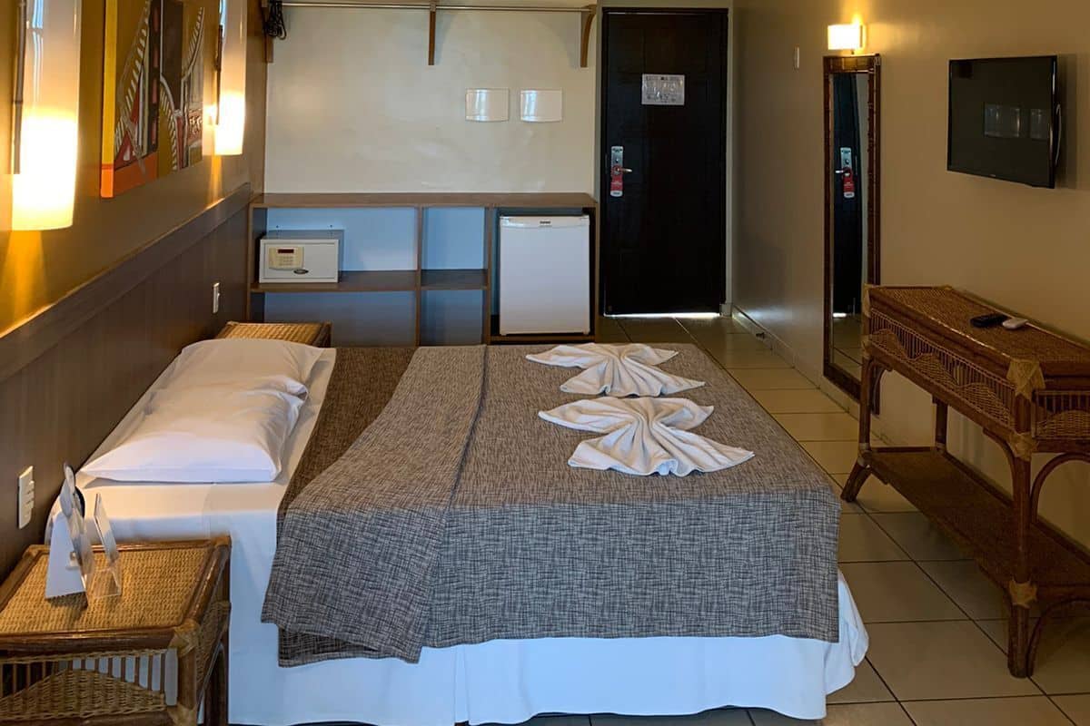 A hotel room with a bed, bedside tables, a desk, a refrigerator, a television, and a door.