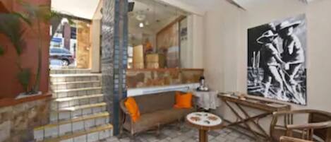Un vestíbulo de hotel con piso a cuadros, un sofá con cojines naranjas, una mesa redonda y un cuadro grande en blanco y negro en la pared.