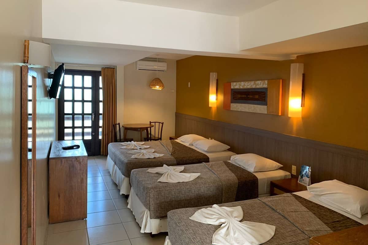 A hotel room with three beds, a desk, a chair, and a dining table.