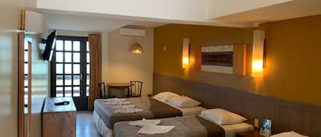 A hotel room with three beds, a desk, a chair, and a dining table.