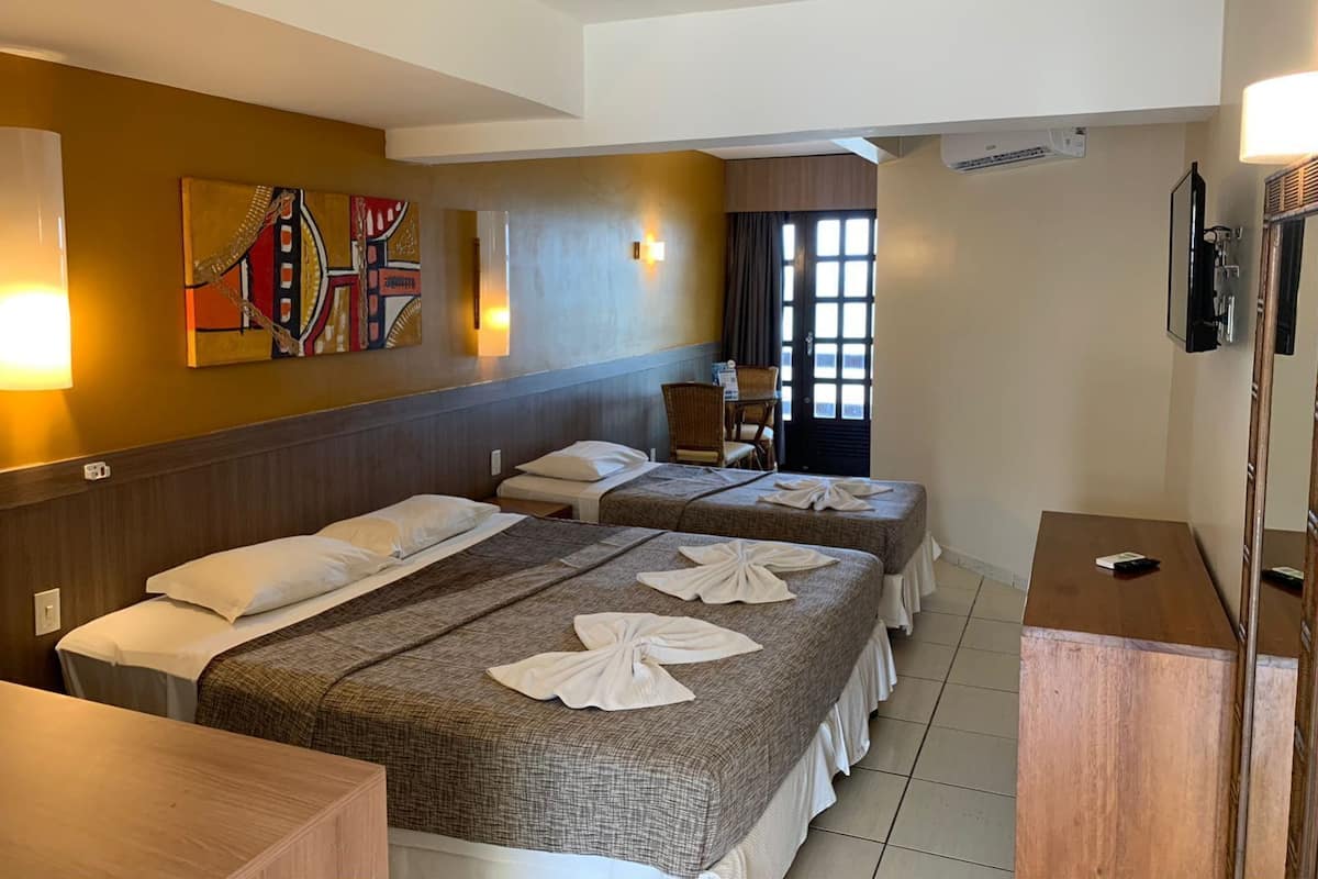 A hotel room with two beds, a wooden headboard, a painting on the wall, a desk, and a TV.
