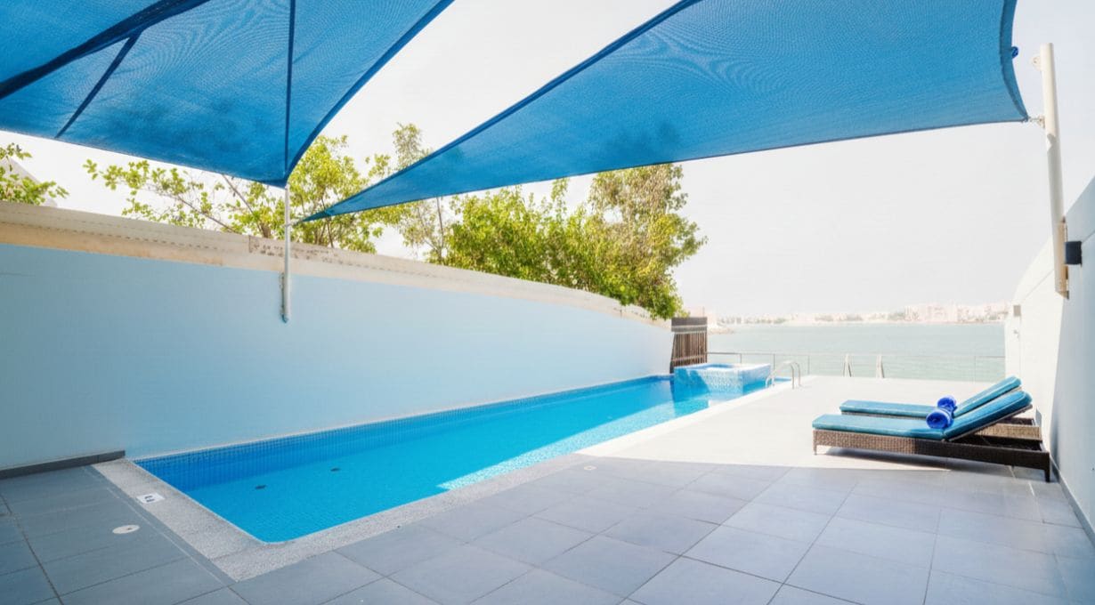 Piscina externa com vista para o mar, área de estar com espreguiçadeiras e zona coberta com toldos azuis.