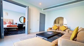 A modern living room with a sofa, a coffee table, and a bed with red patterned pillows. - Dragon Beach Hotel (Amwaj Islands)