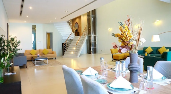 A modern living room with a dining area, a staircase, and a green sofa.