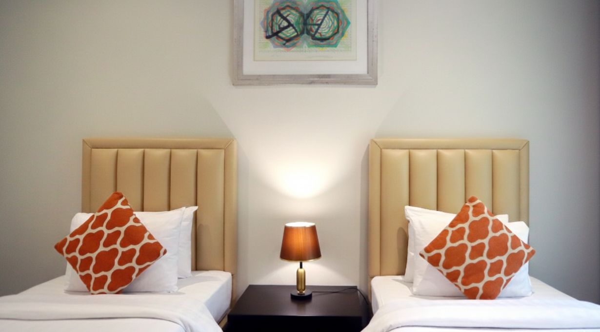 A hotel room with two beds, a nightstand with a lamp, and a framed artwork on the wall.