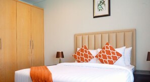 A hotel room with a bed, two nightstands, a wardrobe, and a framed picture on the wall. - Dragon Beach Hotel (Amwaj Islands)