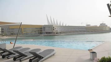 A swimming pool with lounge chairs, a modern building with spire-like architecture in the background, and a clear sky.