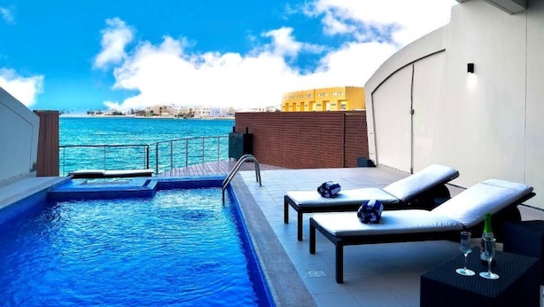 Un espace piscine aménagé sur le toit, offrant une vue sur la mer, avec des chaises longues et une petite table où sont servis des boissons.