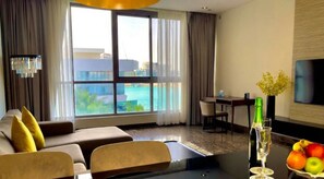 A modern hotel room with a sofa, dining table, and a view of the city and water. - Dragon Beach Hotel (Amwaj Islands)