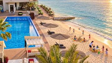 Un complexe hôtelier doté d’une piscine, d’une plage et d’un espace extérieur aménagé avec des sièges.