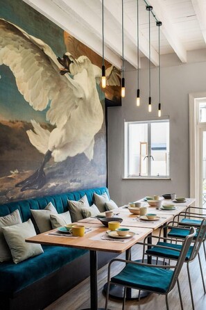 Un espace repas avec une longue table, des chaises et une grande fresque murale représentant un ange.