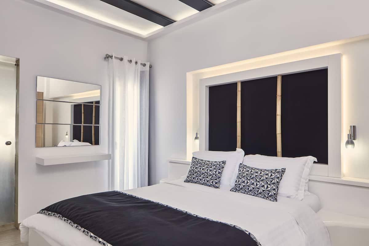 Ein modernes Schlafzimmer mit einem großen Bett, einem Schminkspiegel, einem Fenster mit Verdunkelungsvorhang und einem weißen Nachttisch.