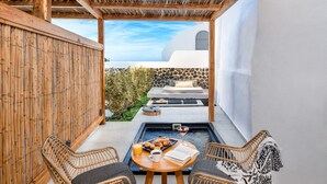 A cozy outdoor seating area with wicker chairs and a table, a small pool, and a view of a white building with a blue sky. - Callia Retreat Adults Only (Santorini)