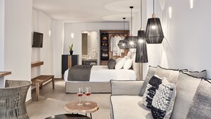 A modern hotel room with a bed, sofa, and a dining area with a table and chairs. - Callia Retreat Adults Only (Santorini)
