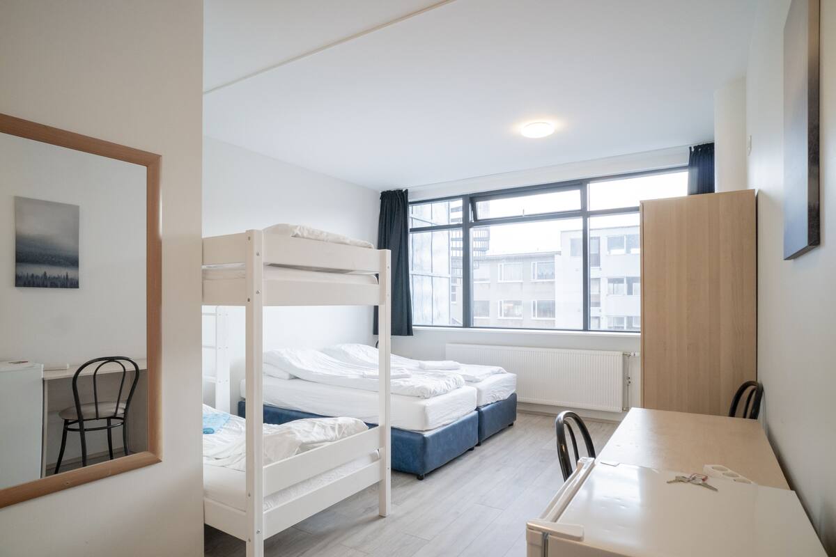 A bedroom with bunk beds, a desk, and a window with a view of buildings.